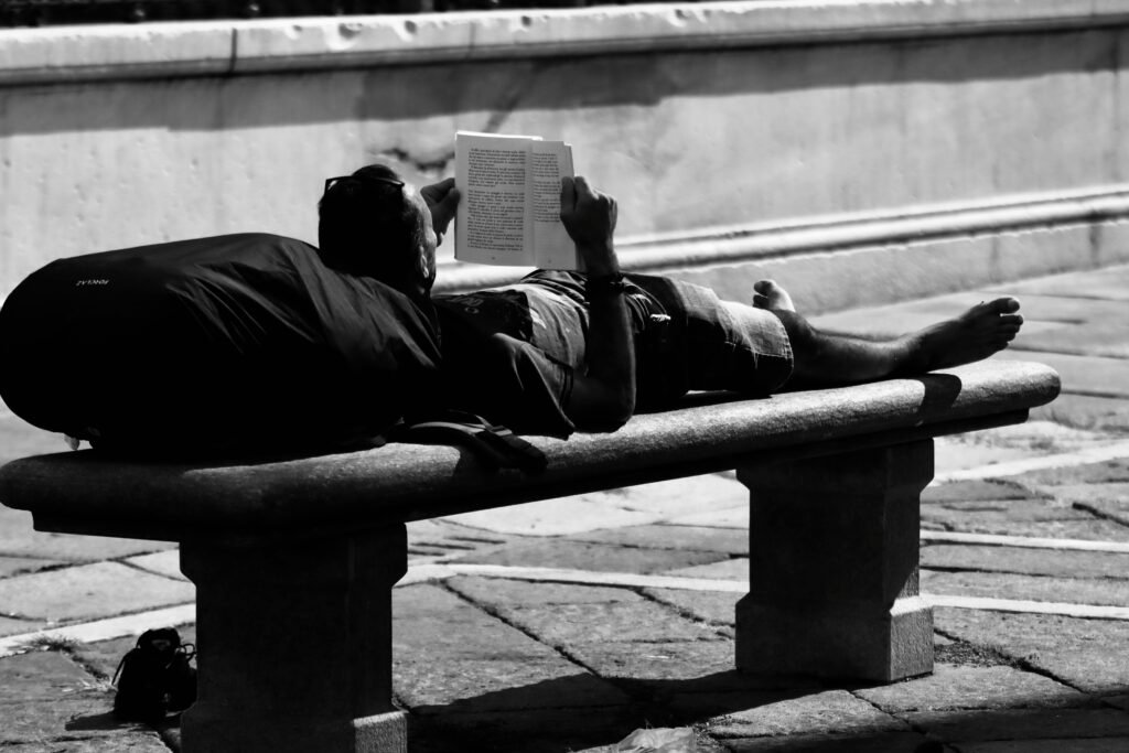 A man relaxes by reading a book on a bench in a Turin street scene.
